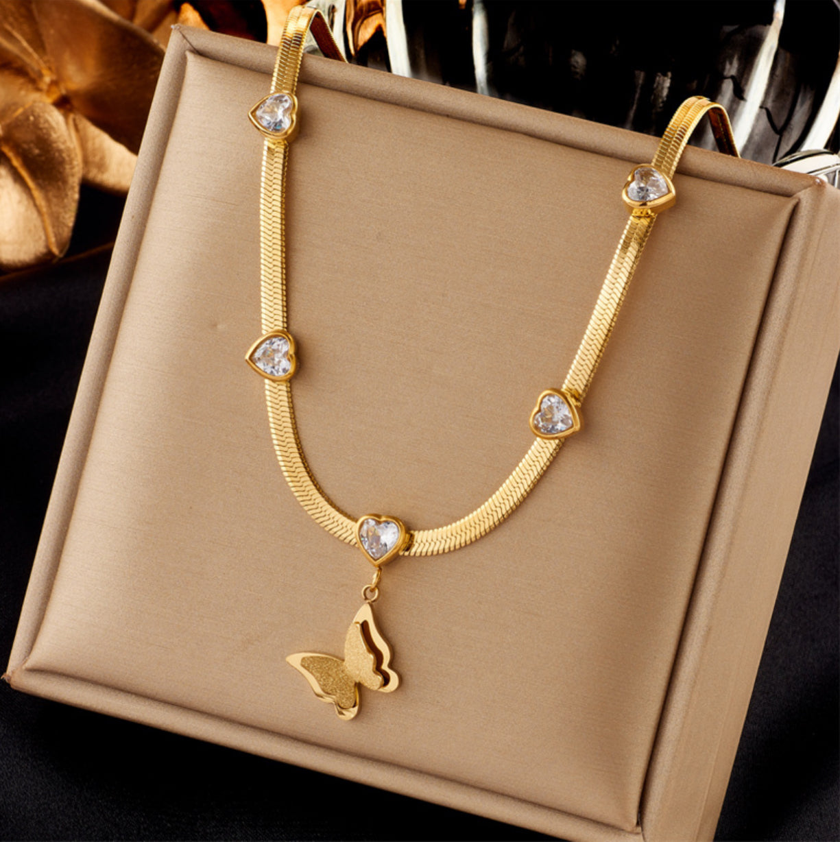 Gold necklace with butterfly pendant on a beige jewelry box