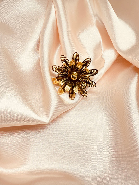 Gold flower-shaped brooch on a soft pink fabric background