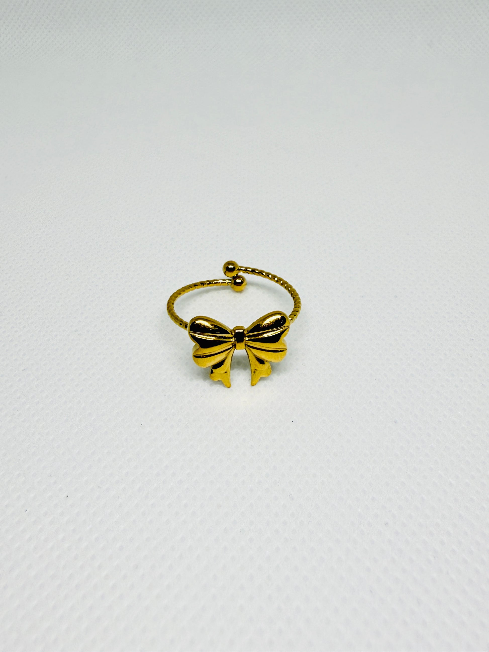 Gold bow-shaped ring on a light gray background