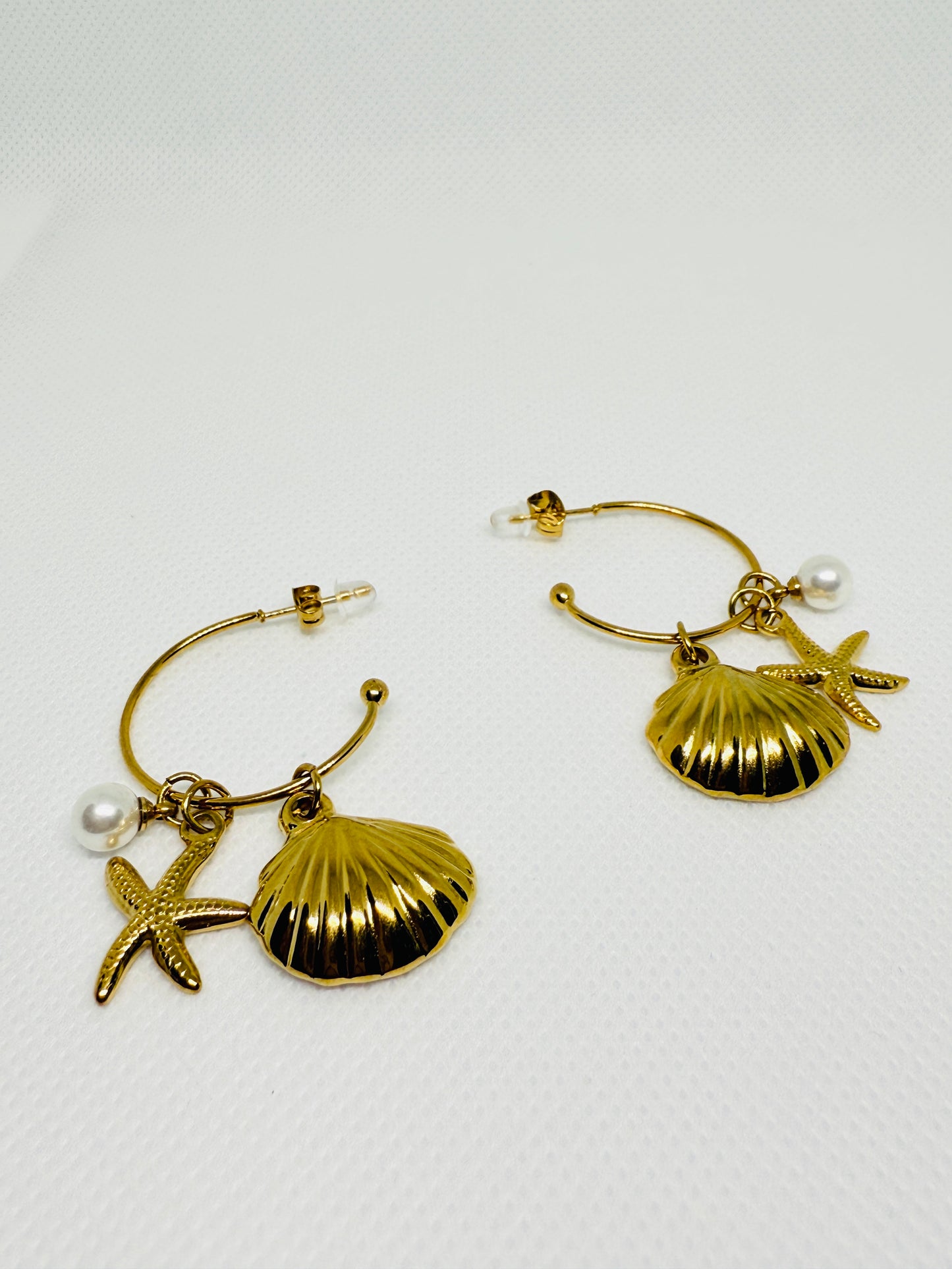 Gold hoop earrings with shell and starfish charms on a white background