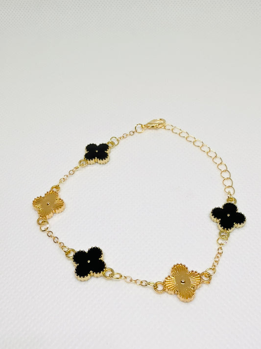 Gold bracelet with black flower-shaped charms on a light gray background