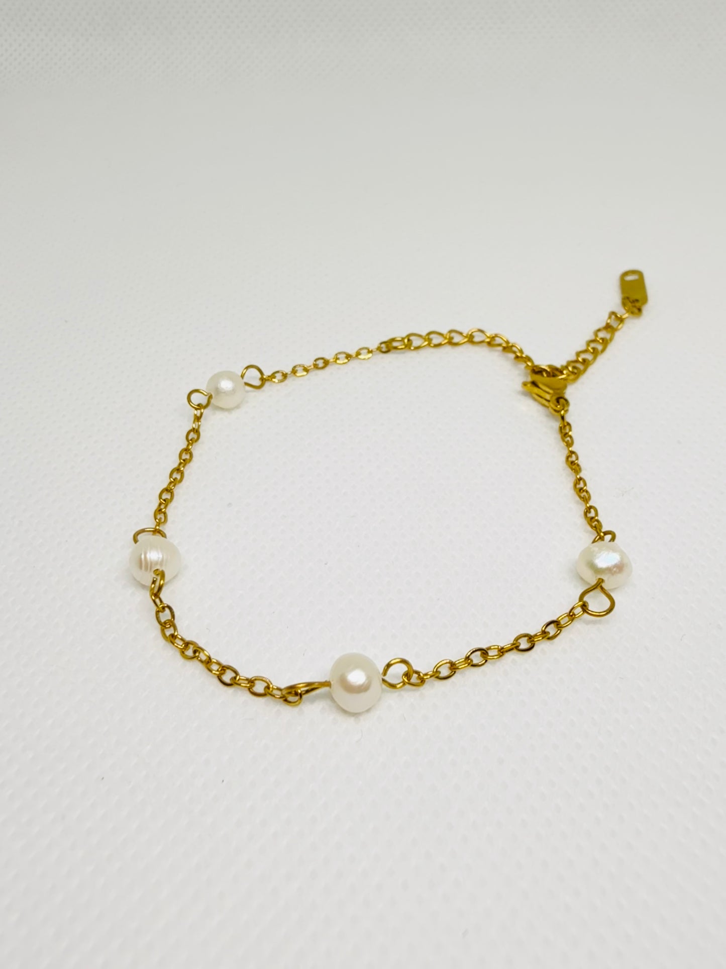 Gold chain bracelet with pearls on a light gray background