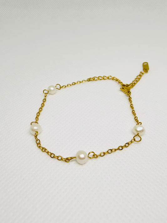 Gold chain bracelet with pearls on a light gray background