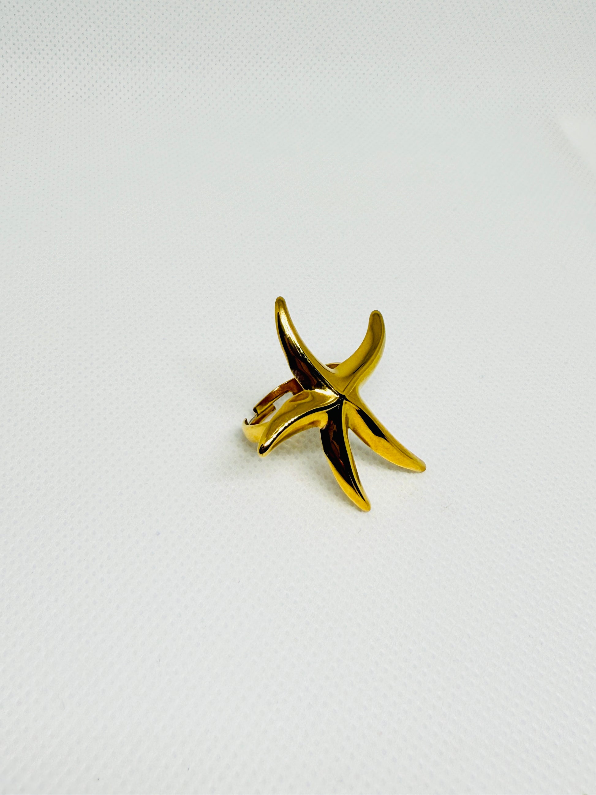 Gold starfish-shaped ring on a light gray background