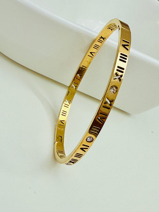 Gold bracelet with Roman numeral design on a white surface