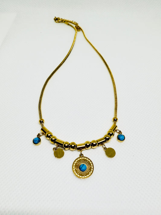 Gold necklace with blue stones and circular pendant on a white background