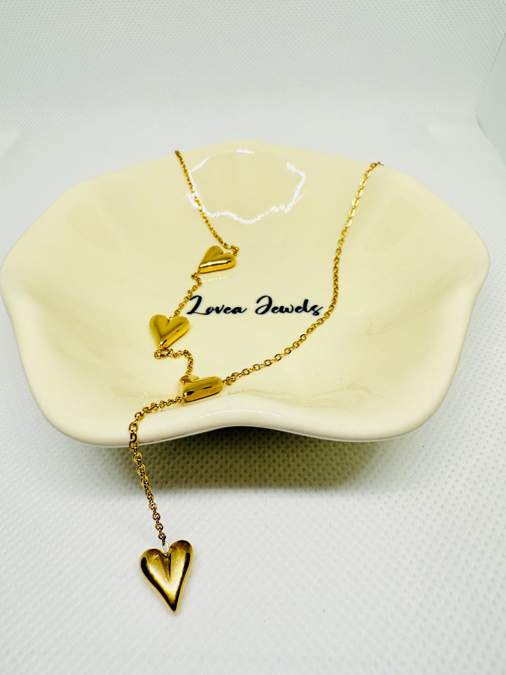 Gold heart-shaped necklace on a white stand with 'Lovera Jewels' branding.
